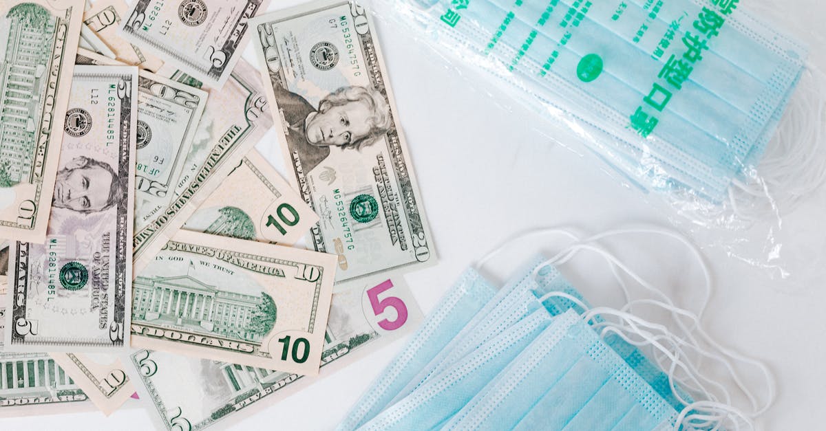 Layover in CDG, traveling from India to US during COVID - From above composition of stack of USA dollar bills placed near medical protective masks produced in China illustrating concept of medical expenses and deficit during COVID 19