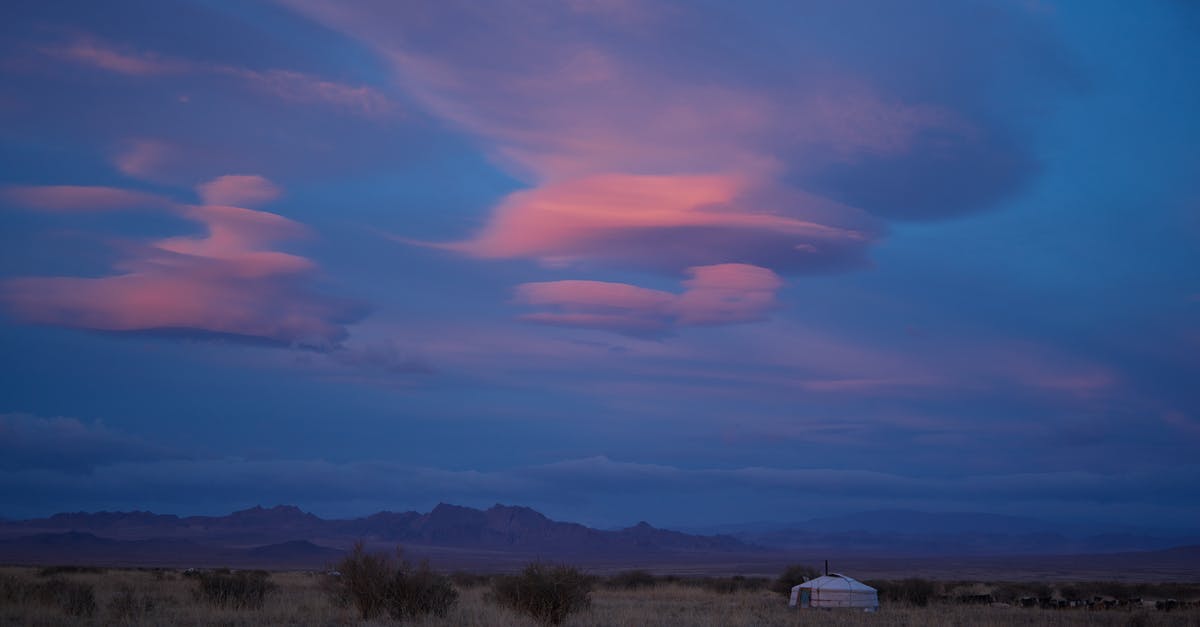 Learning Russian versus Mongolian for visiting Mongolia - Picturesque scenery of pink clouds in dark blue sky under traditional Mongolian ger in prairie with remote mountains during dusk