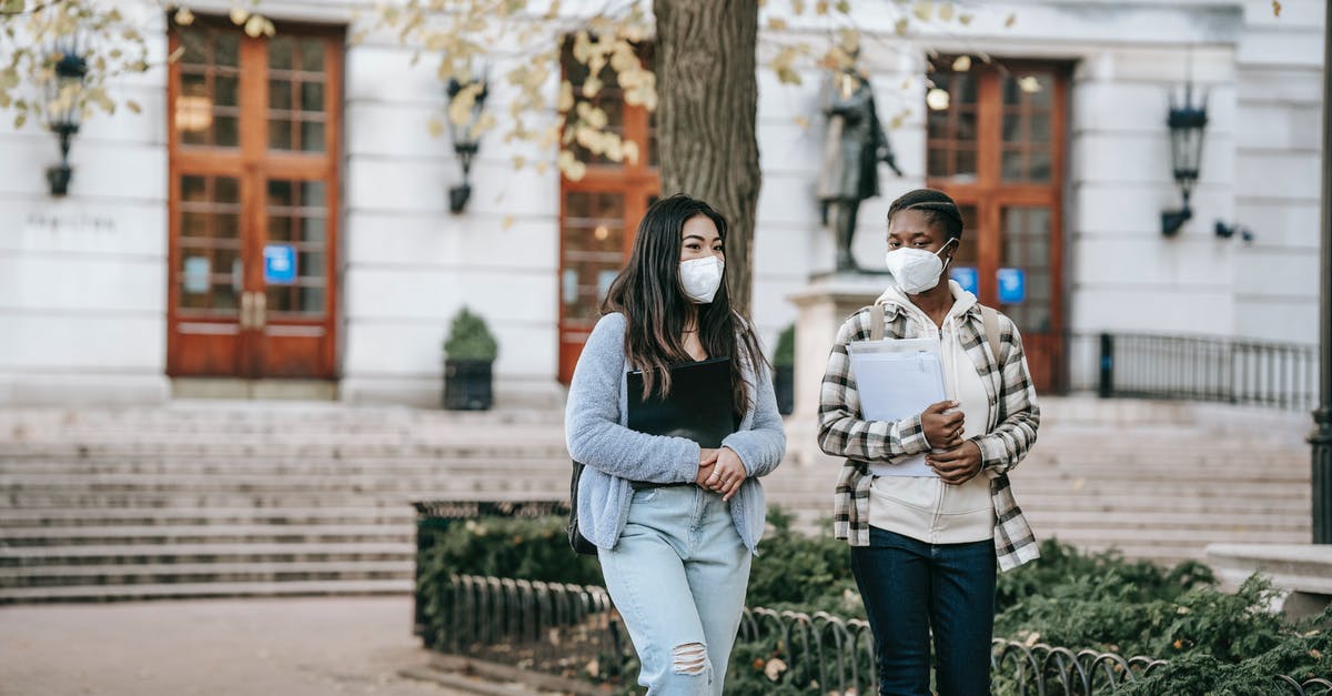 Leaving major cities during COVID-19 pandemic - Young diverse women in respirators walking on street and talking