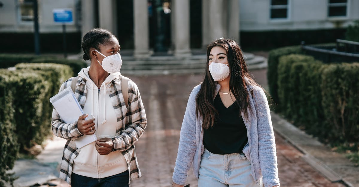 Leaving major cities during COVID-19 pandemic - Diverse women in respirators with folders walking on campus sidewalk