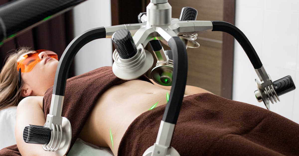 Legalities and safety concerns of visiting prostitutes in Amsterdam - Female client lying on table under lasers of modern weight loss machine on belly during liposuction procedure in medical clinic