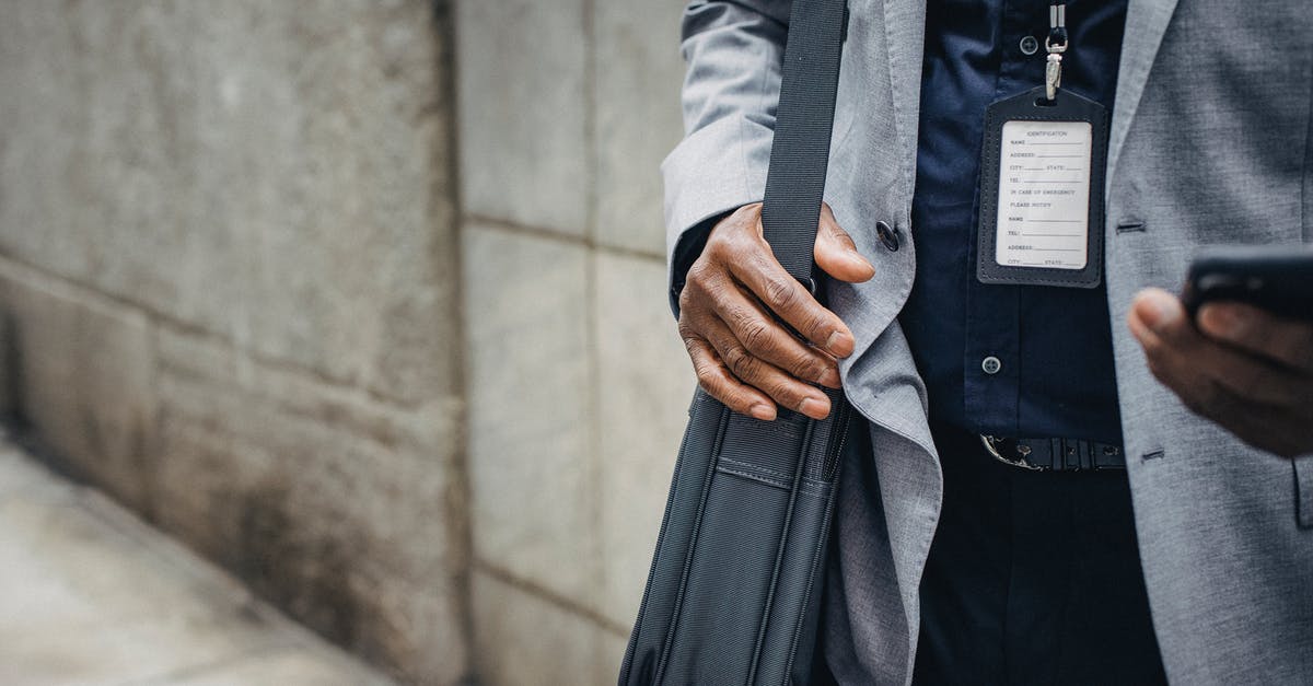 Loading a 1-day pass to a compass card online - Crop anonymous African American entrepreneur in gray jacket with satchel and pass card browsing internet on smartphone on pavement near stone wall in city in daylight