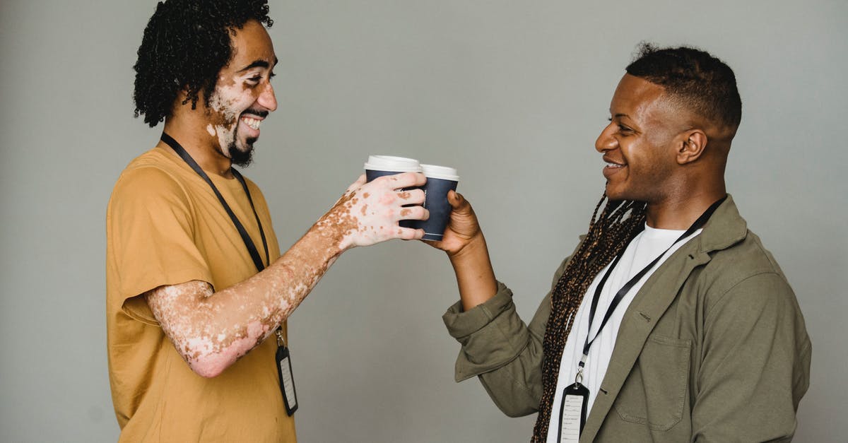 London Oyster Card - unusual requests - Side view of cheerful androgynous man with Afro braids standing on gray background near black coworker with vitiligo skin during coffee break