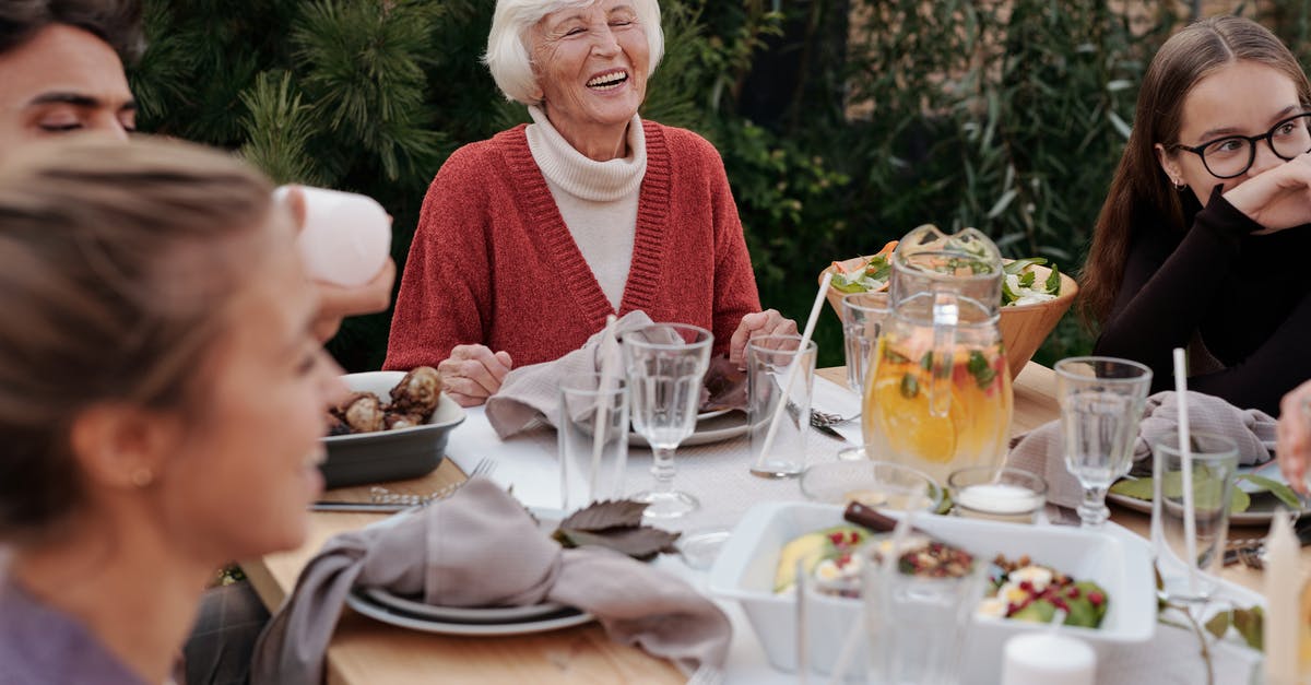 Long layover (22h) for elder relative at BKK airport - Smiling elderly woman with family and friends enjoying dinner at table backyard garden