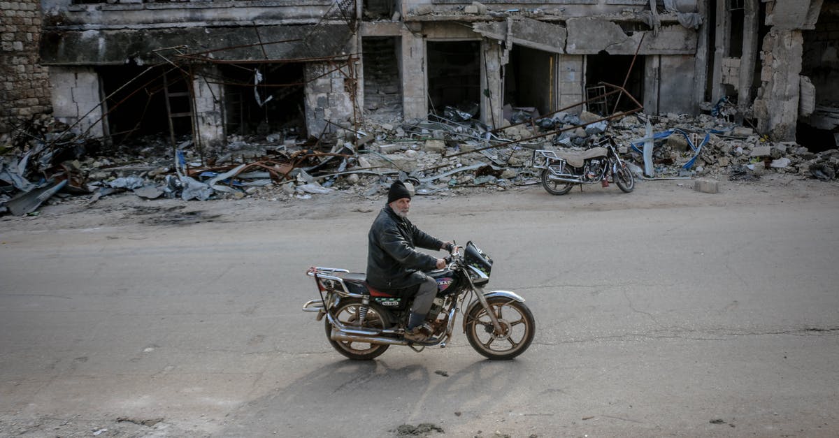 Longest uninhabited road segments - Man riding motorbike along destroyed building