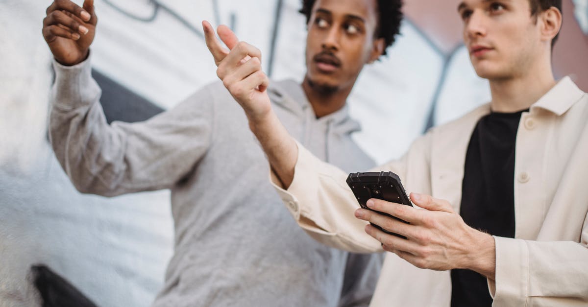 Lost & Found Mobile Telepone - Serious young multiracial men pointing away and using smartphone near graffiti wall