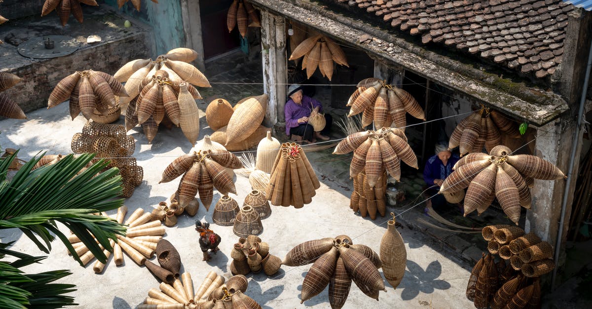 make schengen visa outside your origin country/homeland - From above of people sitting and making bamboo fish traps while working on local bazaar in Vietnam in daylight