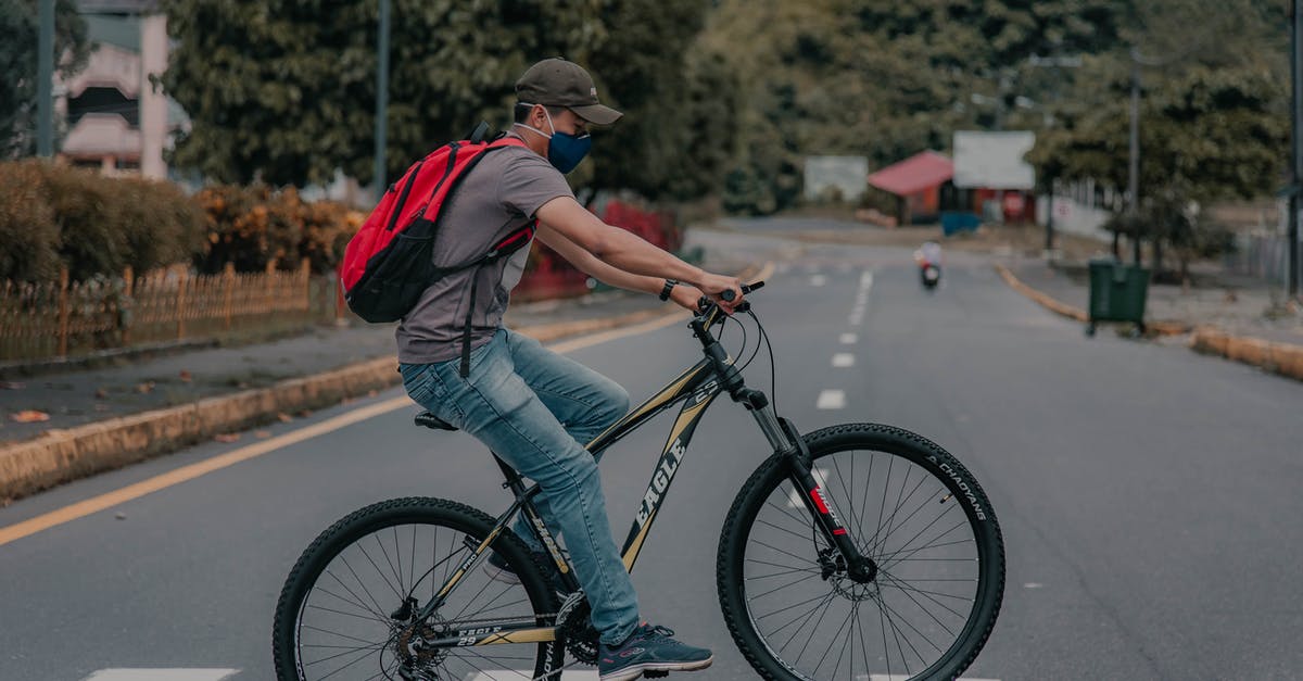 May a cyclist or a pedestrian cross from Switzerland to France near the Basel EuroAirport without going into the airport? - Male in casual clothes cap and backpack wearing face mask cycling on bike on pedestrian crossing