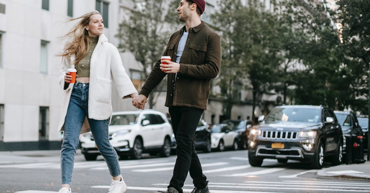 May a cyclist or a pedestrian cross from Switzerland to France near the Basel EuroAirport without going into the airport? - Young couple wearing warm jackets and with paper cups of hot drinks crossing road holding hands and looking at each other