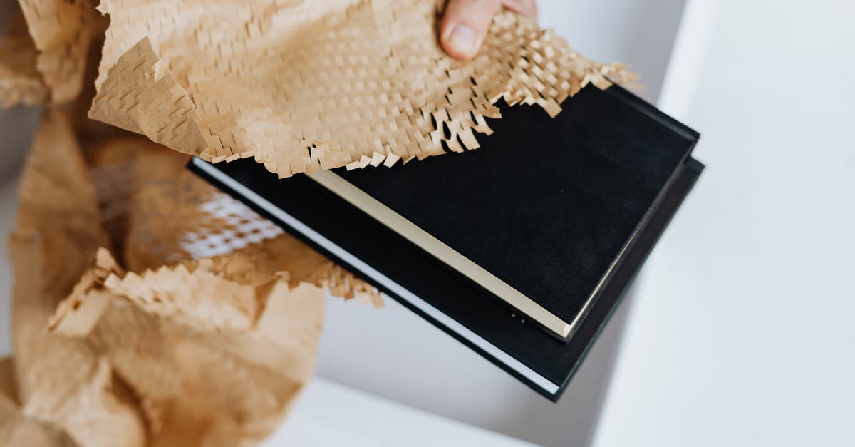 May I take a parcel as my "personal item"? - From above unrecognizable adult male taking black notebooks with craft perforated paper under white carton box while preparing mail delivery at white table