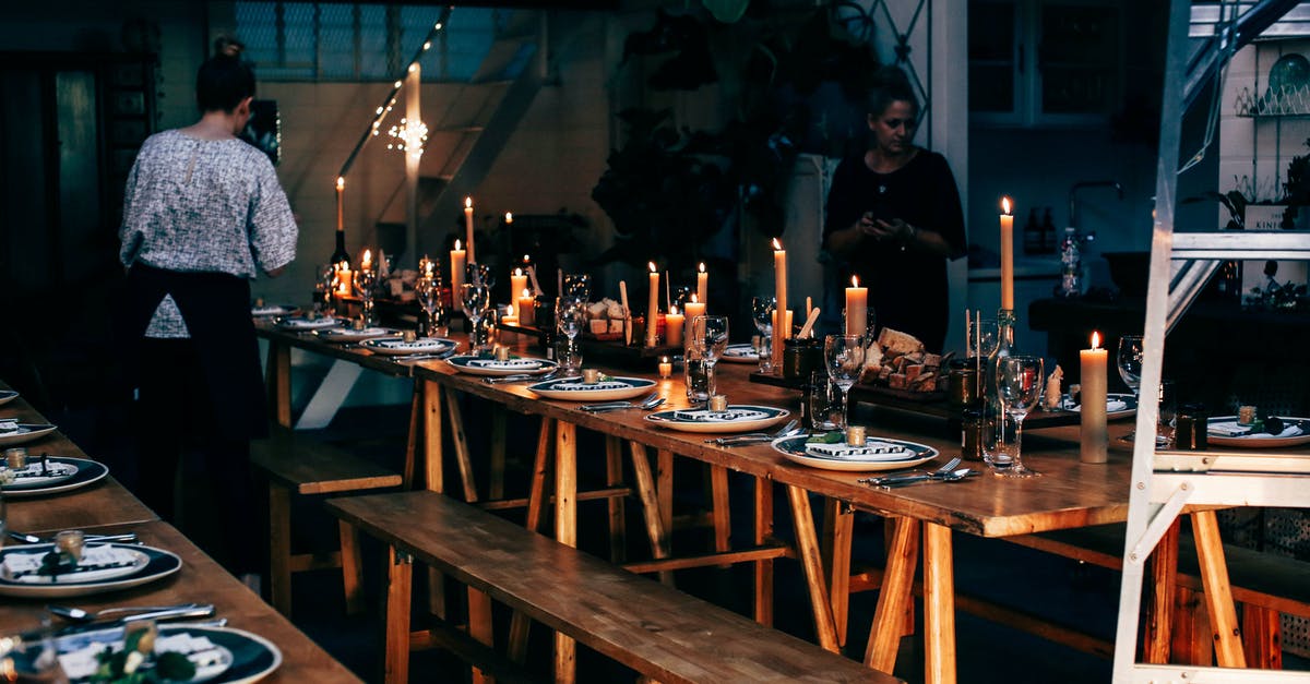 Meeting place in CDG - Anonymous women serving wooden tables with plates and glassware among burning candles while preparing for banquet in modern place