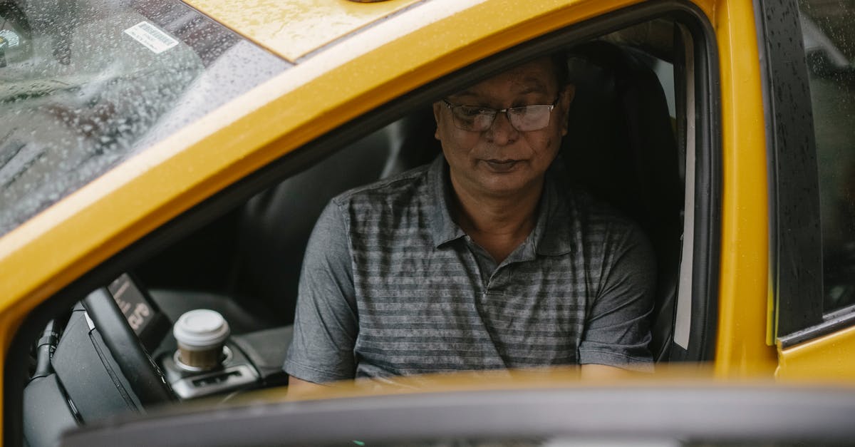 Meta-search engine for licensed taxis - From above of focused Asian taxi driver sitting in wet car with opened door and looking down