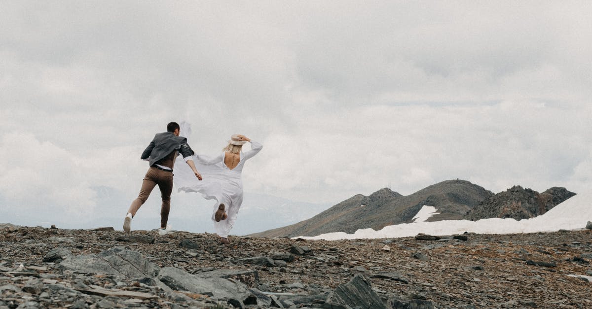 Mexican visa by land versus air - Back view of unrecognizable trendy groom catching up bride in white dress on ridge with snow on wedding day