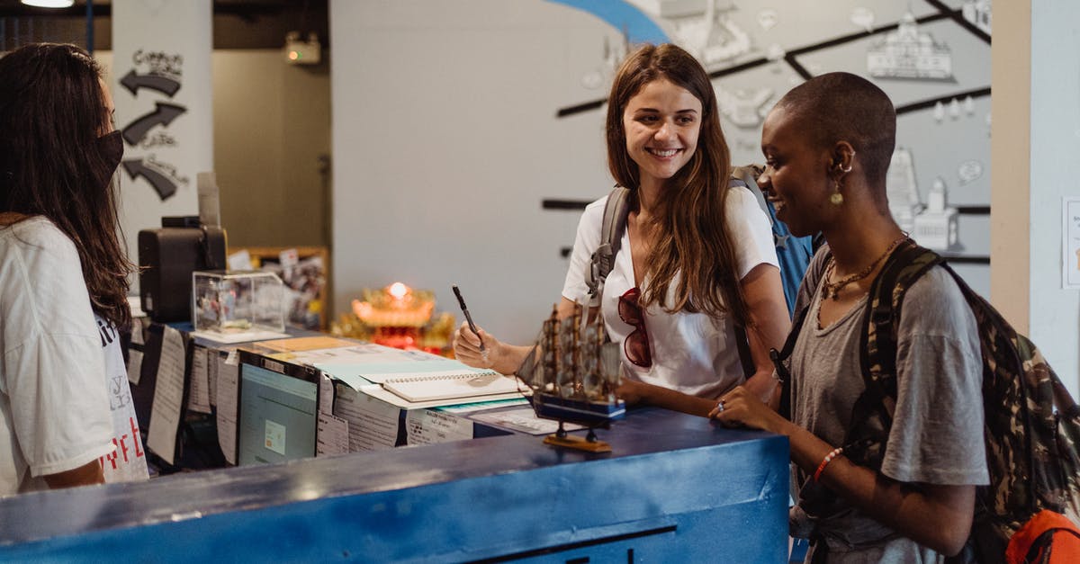 Midnight check-in: Hostel in Paris - Two Women with Backpacks Smiling Beside Blue Desk