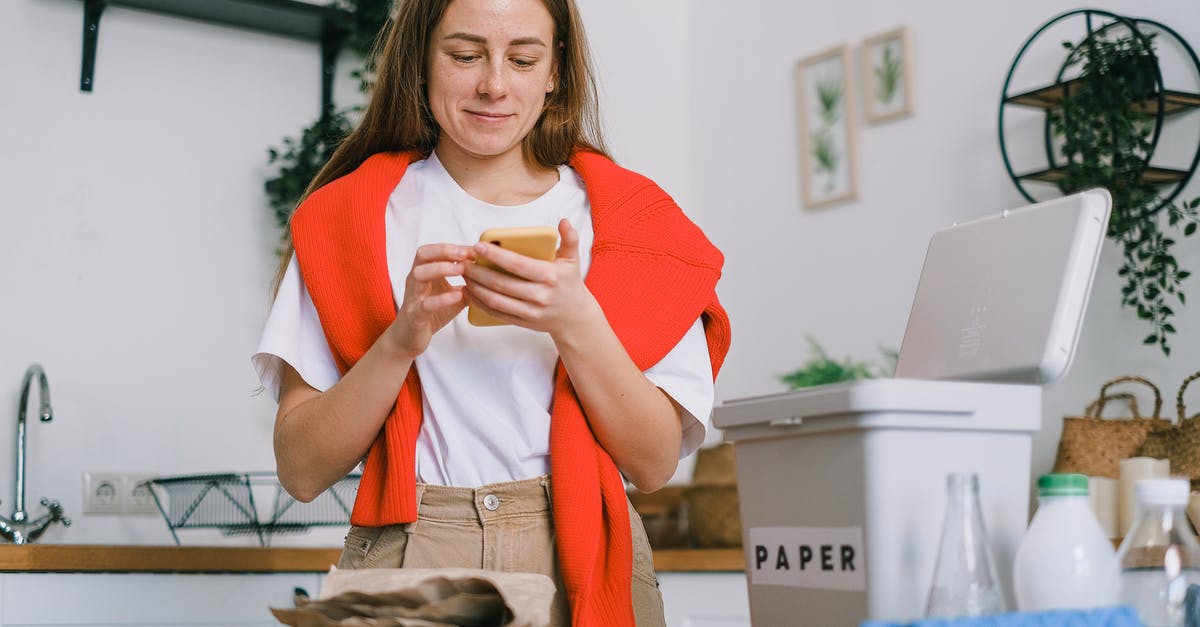 Mobile apps as alternative to paper boarding pass - Cheerful female browsing mobile phone and standing at table with sorted paper and plastic waste