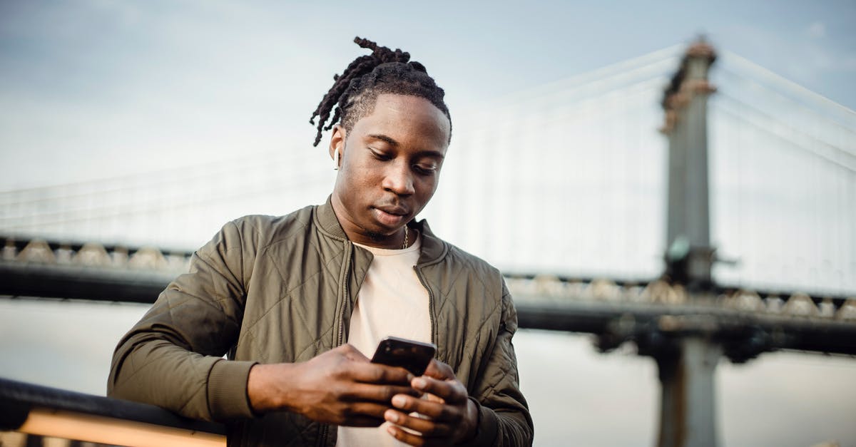 Mobile connectivity in Israel, in and outside small and large cities? - From below of serious black man in earphones scrolling smartphone while listening to music outside and looking down