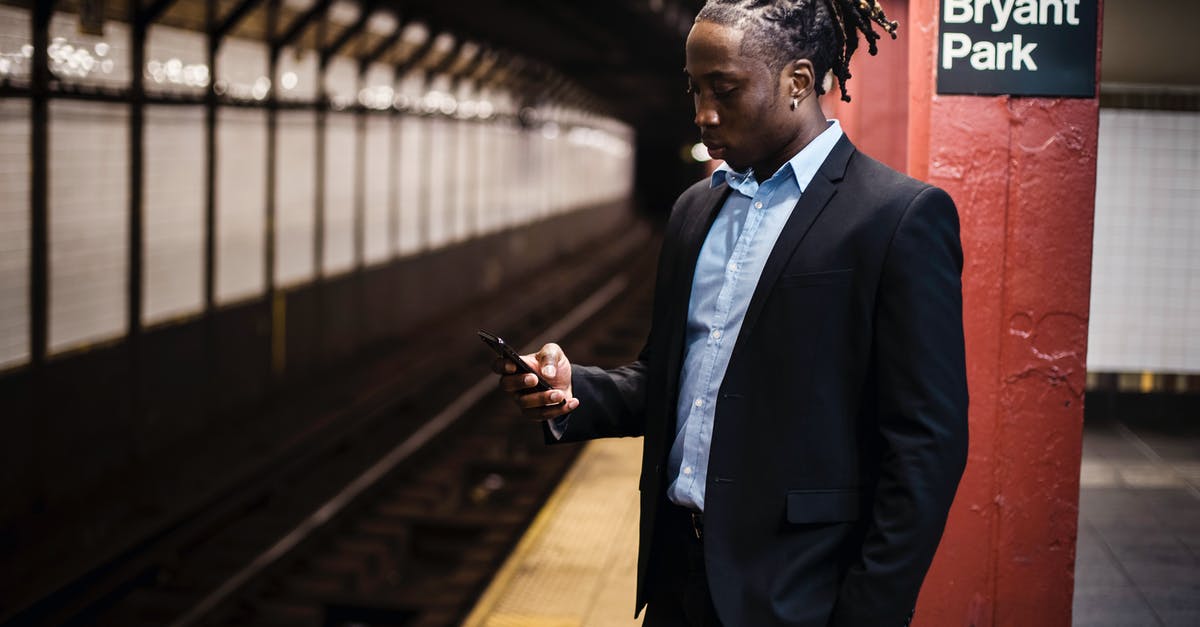 Mobile internet in New York City - Modern young African American man in office suit text messaging on cellphone while waiting for train at Manhattan subway station