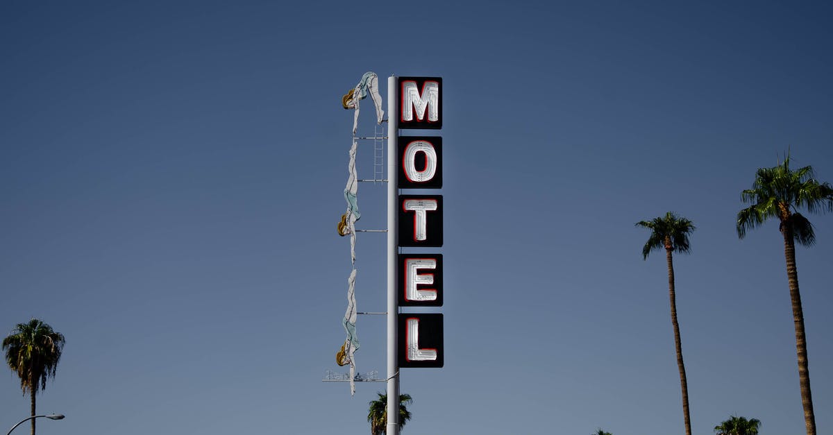 Motel on Route 66 in California, 1963 - Low angle of motel signboard on metal pillar located at roadside near tall palms against cloudless blue sky