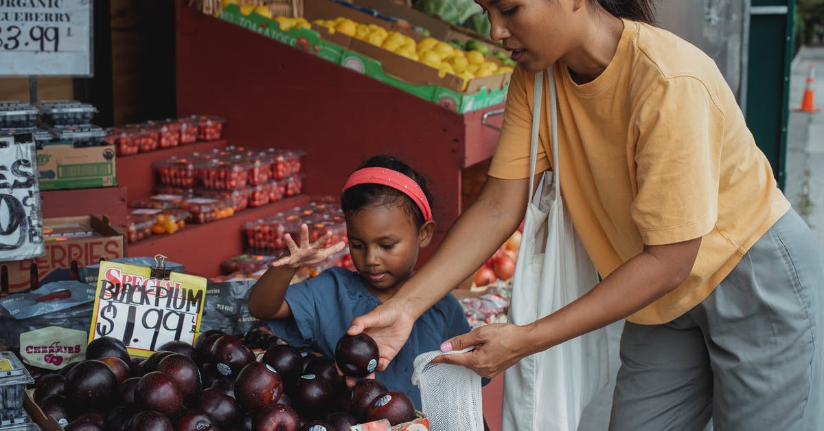 Mother name is different on my passport [closed] - Asian woman putting black plum into eco bag while choosing fruits from box in street market with daughter