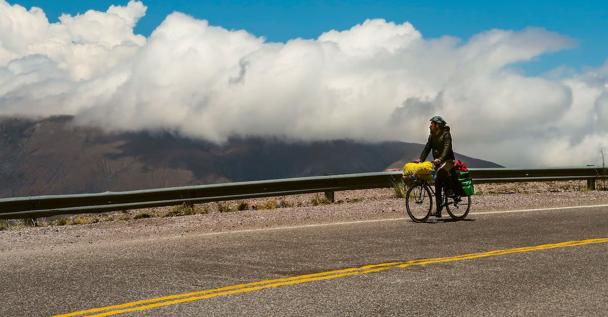 Mountain bike routes in Val di Sole, Trentino? - Unrecognizable guy in warm clothes and helmet riding bicycle on asphalt road with flowers in basket and admiring amazing scenery of clouds over mountains