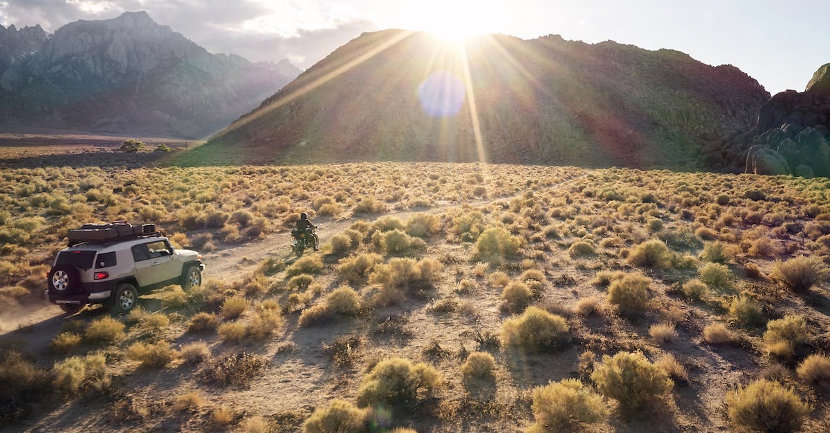 Mountain bike routes in Val di Sole, Trentino? - From above picturesque view of highland semidesert area in evening sun with jeep and bike driving on rural road towards hills