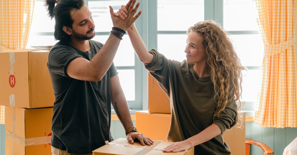 Moving from one SkyTeam partner to another - Happy woman in casual wear standing near heap of cardboard boxes and giving high five to ethnic boyfriend with ponytail showing agreement while looking at each other