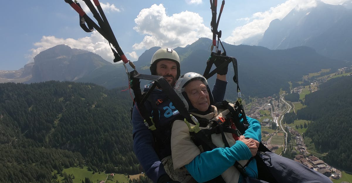 Multiple flight changes - any risk? - Smiling elderly male in protective helmet near young trainer parachuting over mounts under cloudy sky