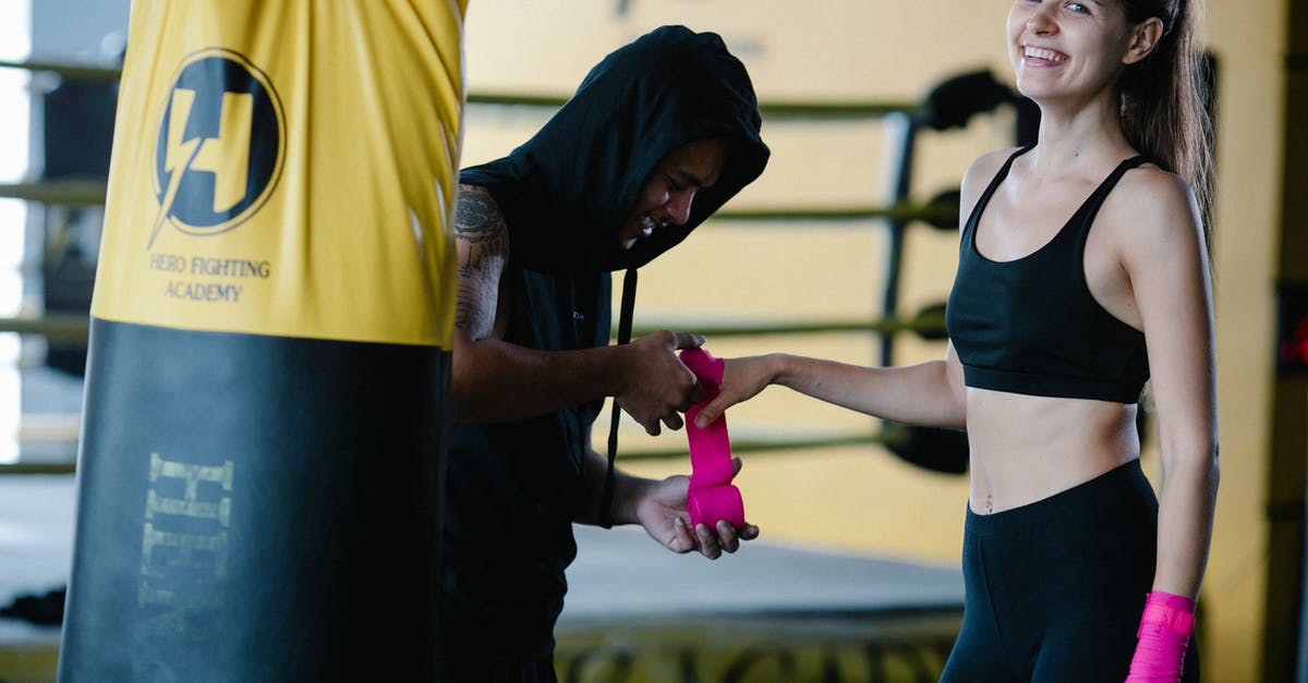 Must I pre-book bag wrap ar LHR? - Personal instructor wrapping pink boxing bandage on hand of smiling sportive female looking at camera during workout in gym with punching bag