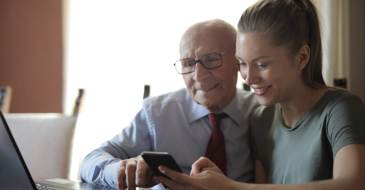 My Granddaughter got bedbugs in a hostel. [closed] - Positive senior man in formal shirt and eyeglasses and smiling young granddaughter sharing mobile phone while sitting near laptop at table