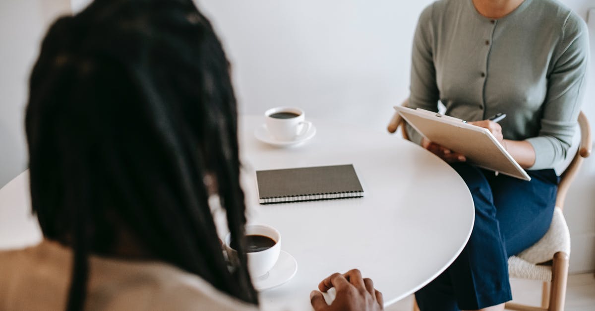 Need advice for UK landing interview (visa-free entry) - Professional ethnic female psychotherapist asking questions to black male patient and taking notes in clipboard while sitting together at table in modern psychotherapy center