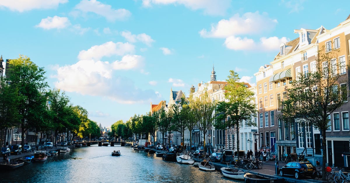 Netherlands visa and bank statement - Magnificent cityscape of Amsterdam with traditional boats moored on calm river near historic buildings under cloudy blue sky