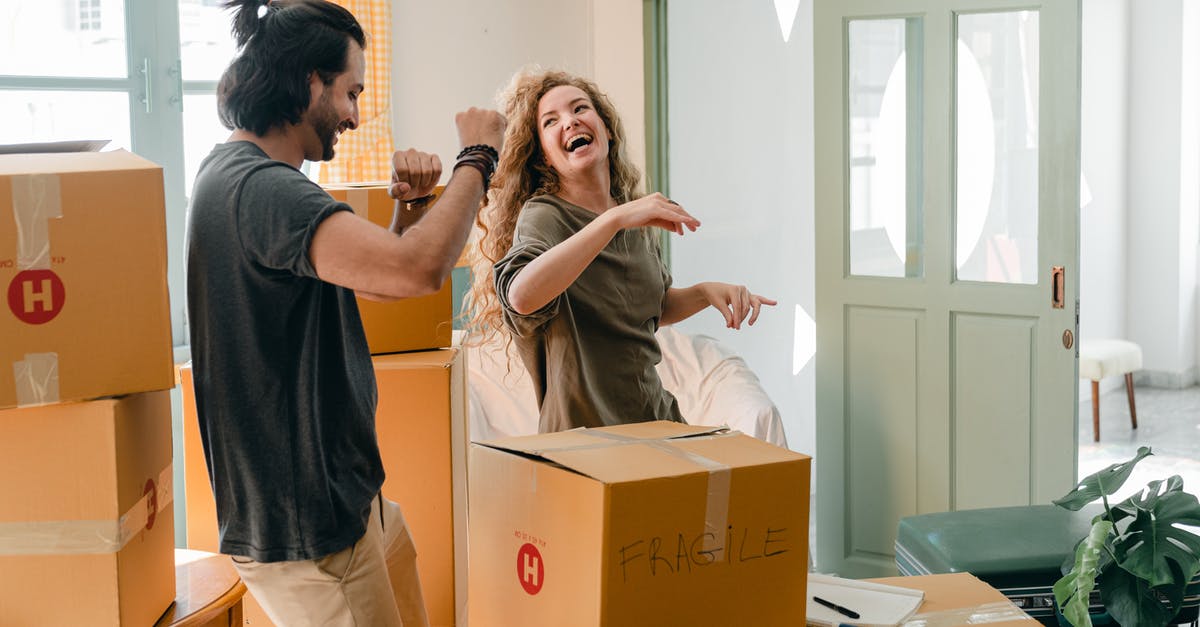 New Zealand boyfriend traveling to Iran with me - Cheerful laughing couple in casual clothes having fun and dancing together while unpacking carton boxes after moving into new contemporary apartment