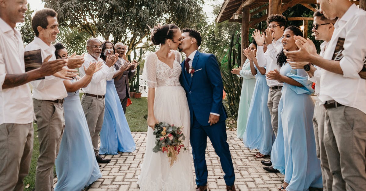 Newly married last name change for wife? [closed] - Young bride with flower bouquet kissing black husband between cheerful clapping guests on tiled walkway during festive event