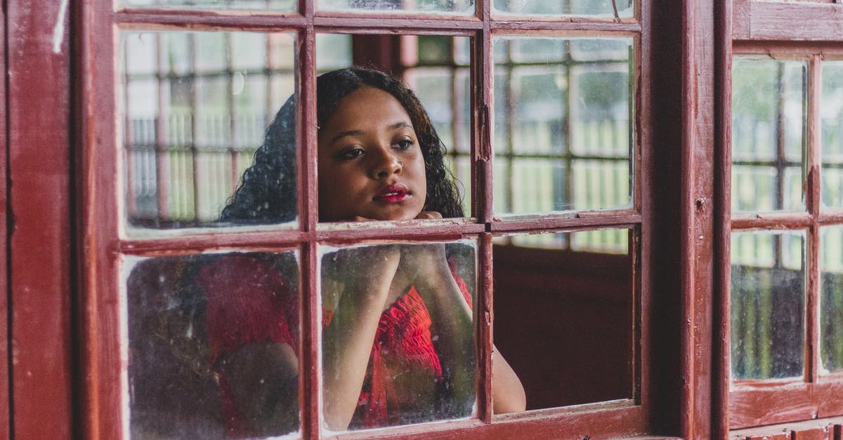 Next day visa - Wait five minutes to enter? - Pensive young ethnic female with wavy hair leaning head on fists while standing near window and dreamily looking through glass away in daytime