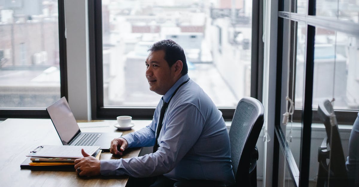 NOC from employer for Schengen visa - High angle side view of smiling ethnic businessman sitting in armchair at table with netbook and documents