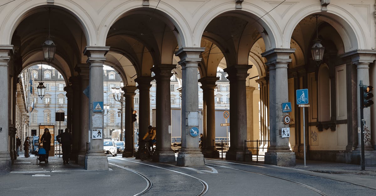 Non-EU citizen in Europe - Unrecognizable citizens on asphalt roadway with tram rails under aged masonry construction with arches and colonnade in city