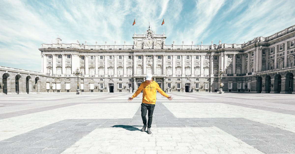 Non-EU family member travelling alone to Spain - Full body of unrecognizable male traveler in casual clothes and cap standing on empty square near Royal Palace of Madrid during holiday in Spain