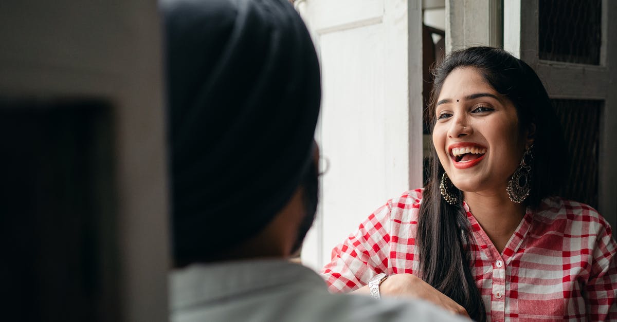 Non-EU married to Dutch citizen, EU Free Movement Visa? - Excited young attractive female with bindi on forehead wearing large earrings with authentic design and checkered cloth sitting in doorway with blurred husband wearing turban during free time