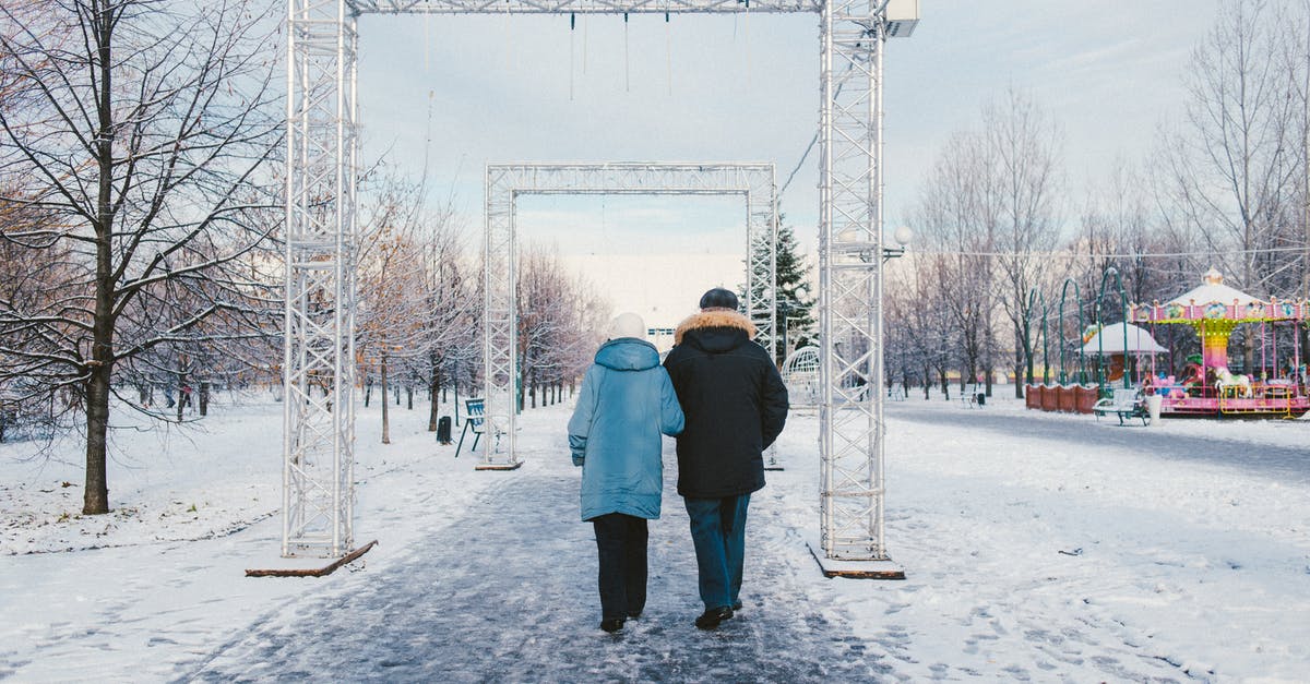 North Korean themed theme parks - Back view of anonymous couple strolling on snowy walkway with rectangular shaped arches in amusement park in town