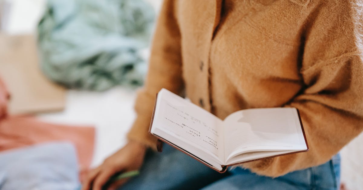 Not able to read bus schedule in France - Crop anonymous female in casual clothes reading notes in notebook while sitting on floor in light room