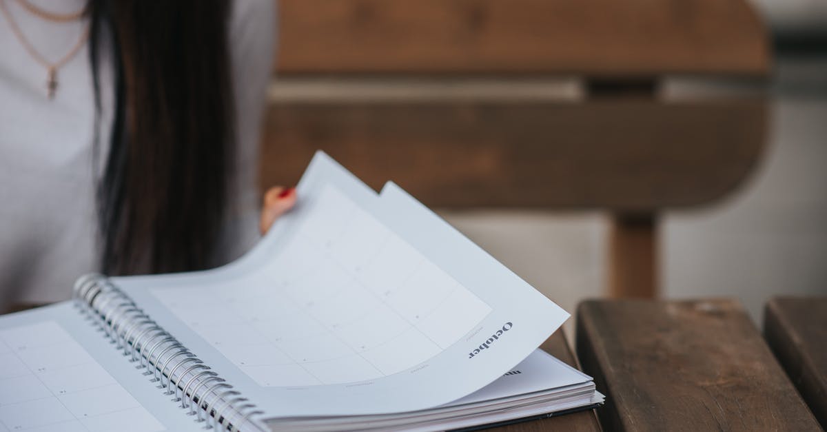 Not able to read bus schedule in France - Crop unrecognizable female student with dark hair in white blouse turning pages of notepad at wooden table in park