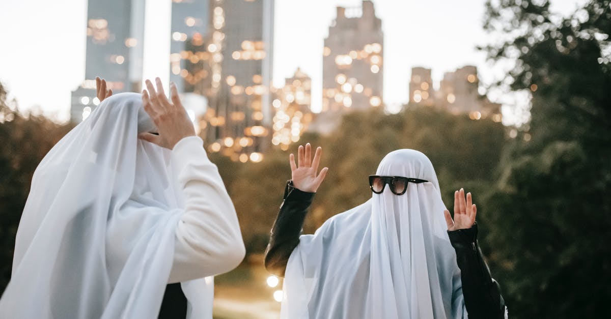 Odd, funky festivals in the Northeast of the US? - Funny unrecognizable couple with raised arms wearing ghost costumes and sunglasses looking at each other while standing in park with glowing skyscrapers on blurred background during Halloween