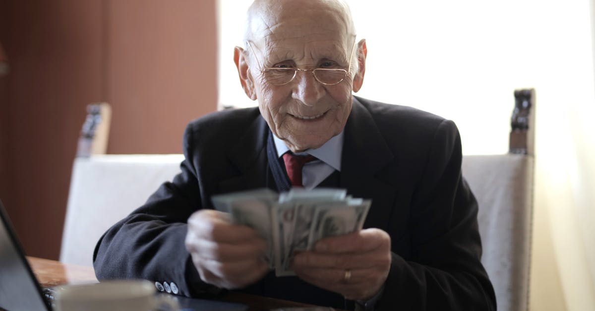 Old paper Canadian currency - Positive senior businessman in formal suit and eyeglasses counting money bills while sitting at wooden table with cup of beverage and near opened laptop