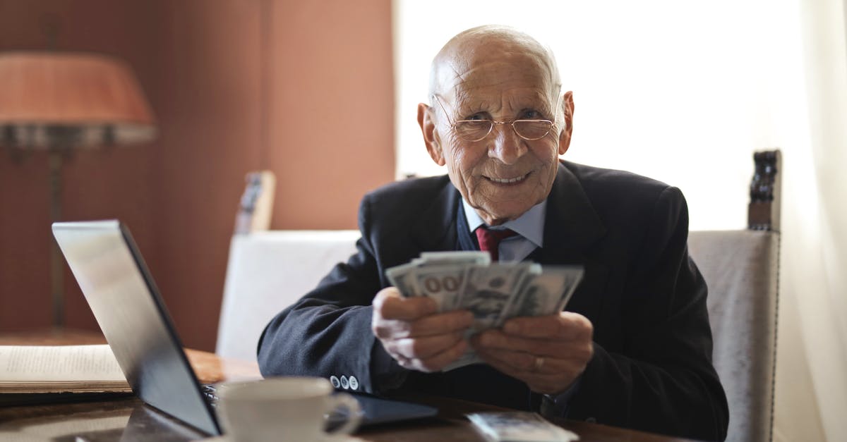 Old paper Canadian currency - Confident senior businessman holding money in hands while sitting at table near laptop