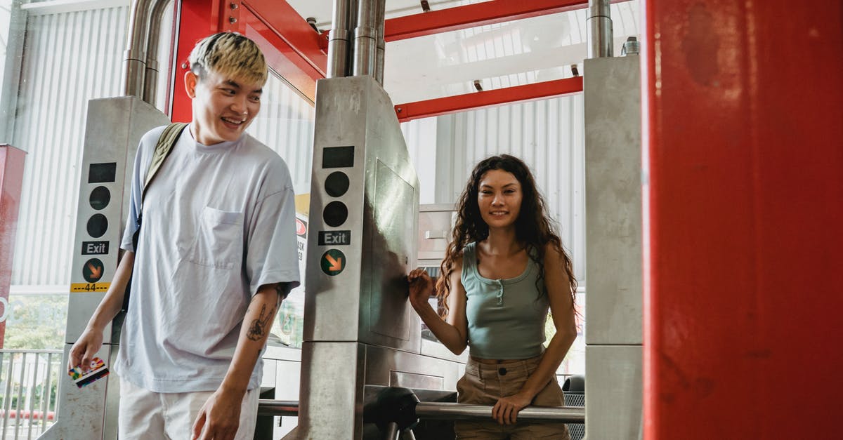 On attempting reentry with tourist pass after being rejected - Young cheerful multiethnic couple of travelers in casual apparel passing through metal barrier gates in daylight