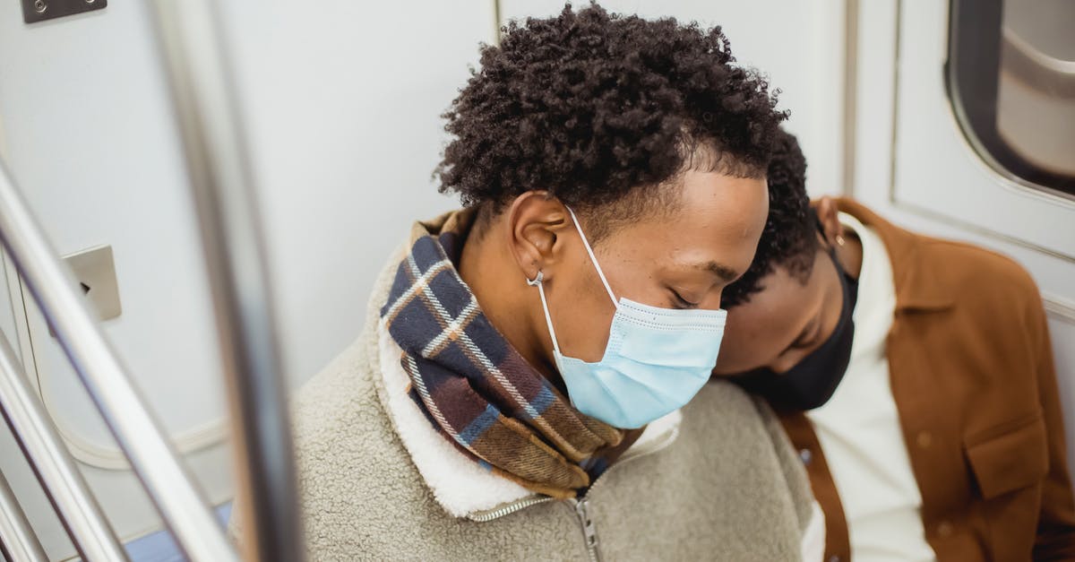 One-way train from Paris to Barcelona [closed] - From above of African American homosexual couple wearing casual clothes in protective masks sleeping while riding in subway train together