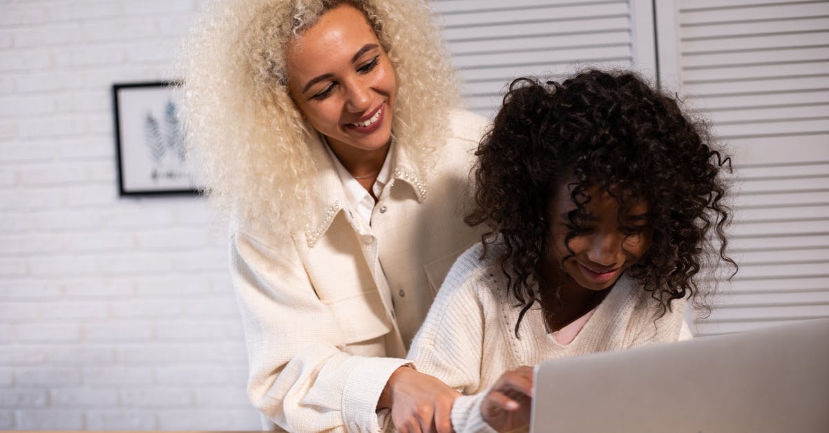 Online boarding passes for Star Alliance connecting flights - Smiling African American woman and girl browsing contemporary netbook while standing at wooden kitchen counter with cut carrot in kitchen