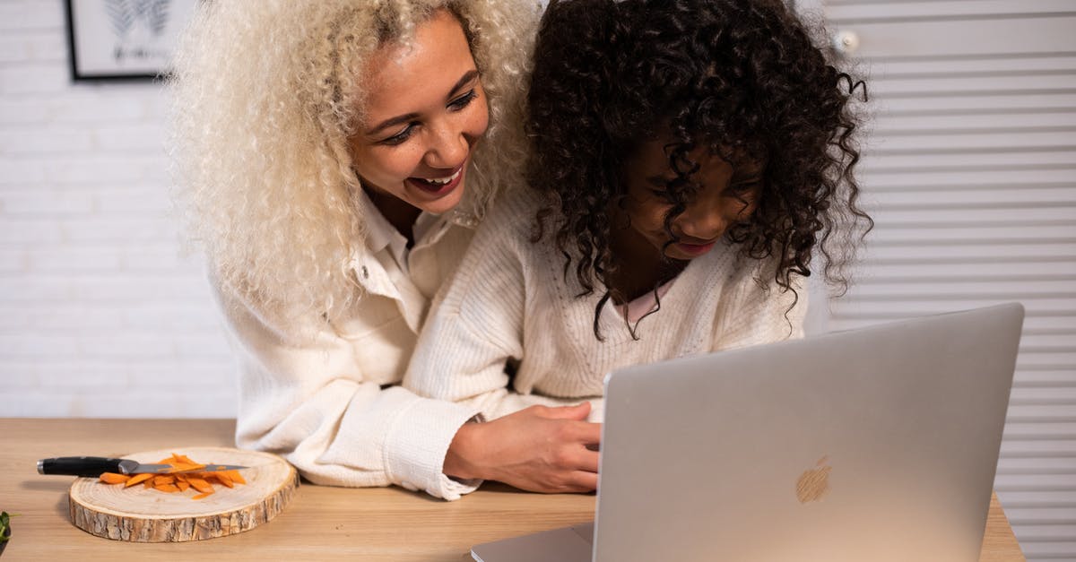 Online boarding passes for Star Alliance connecting flights - Smiling African American woman and girl looking at screen while surfing contemporary netbook at counter with cut carrot in kitchen