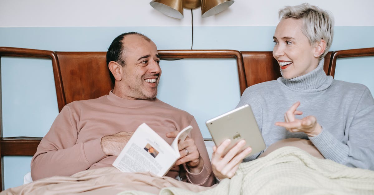 Online flight tickets booking for others - charge additional booking fee - Cheerful diverse couple relaxing in bed with book and tablet during lazy weekend