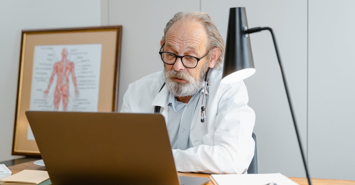 Online medical insurance for short visa in Romania - An Elderly Man in White Lab Coat Talking while Facing the Laptop